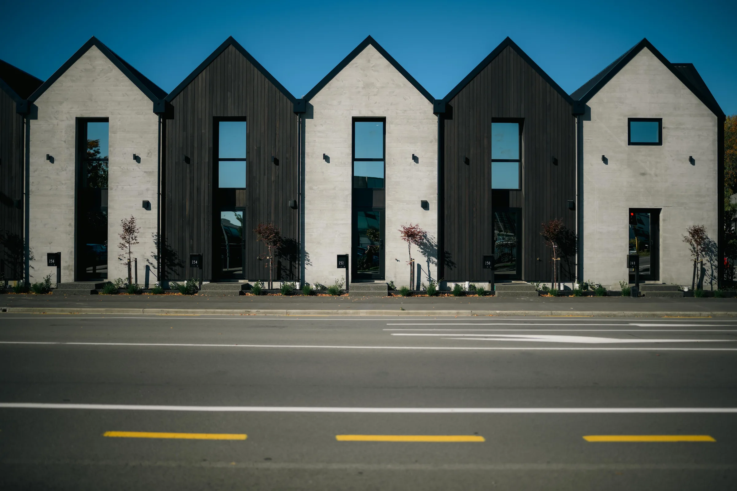 Row of modern townhouses with alternating dark and light facades facing a paved street.