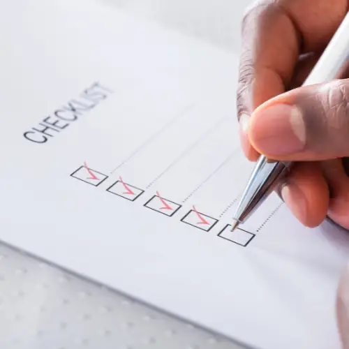 Hand holding a pen checking off the last box on a checklist with four boxes already marked.