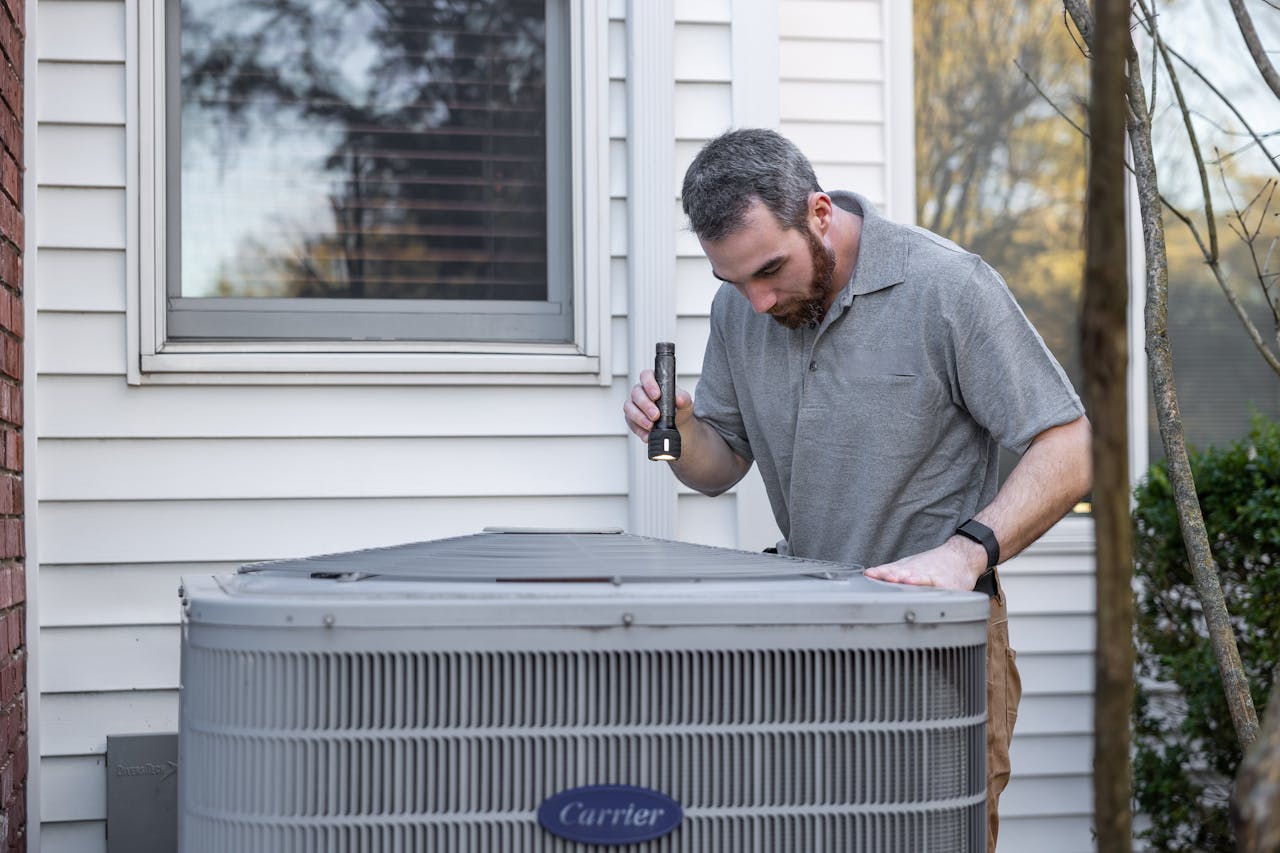 Technician inspecting a Carrier air conditioning unit outdoors using a flashlight.
