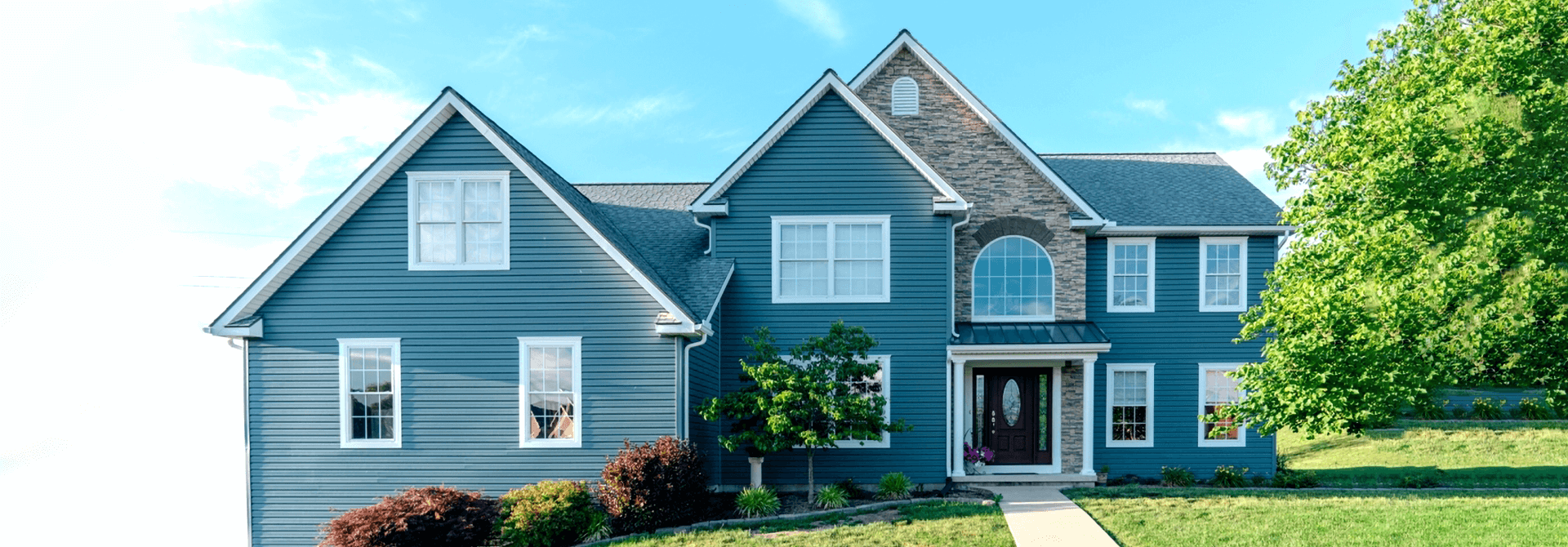 Built two-story blue house with white-trimmed windows, stone accent around entrance.