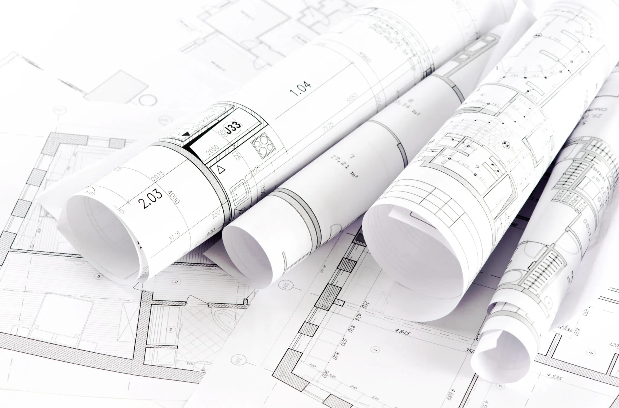 Rolled architectural blueprints placed on flat blueprints with detailed floor plans and measurements.