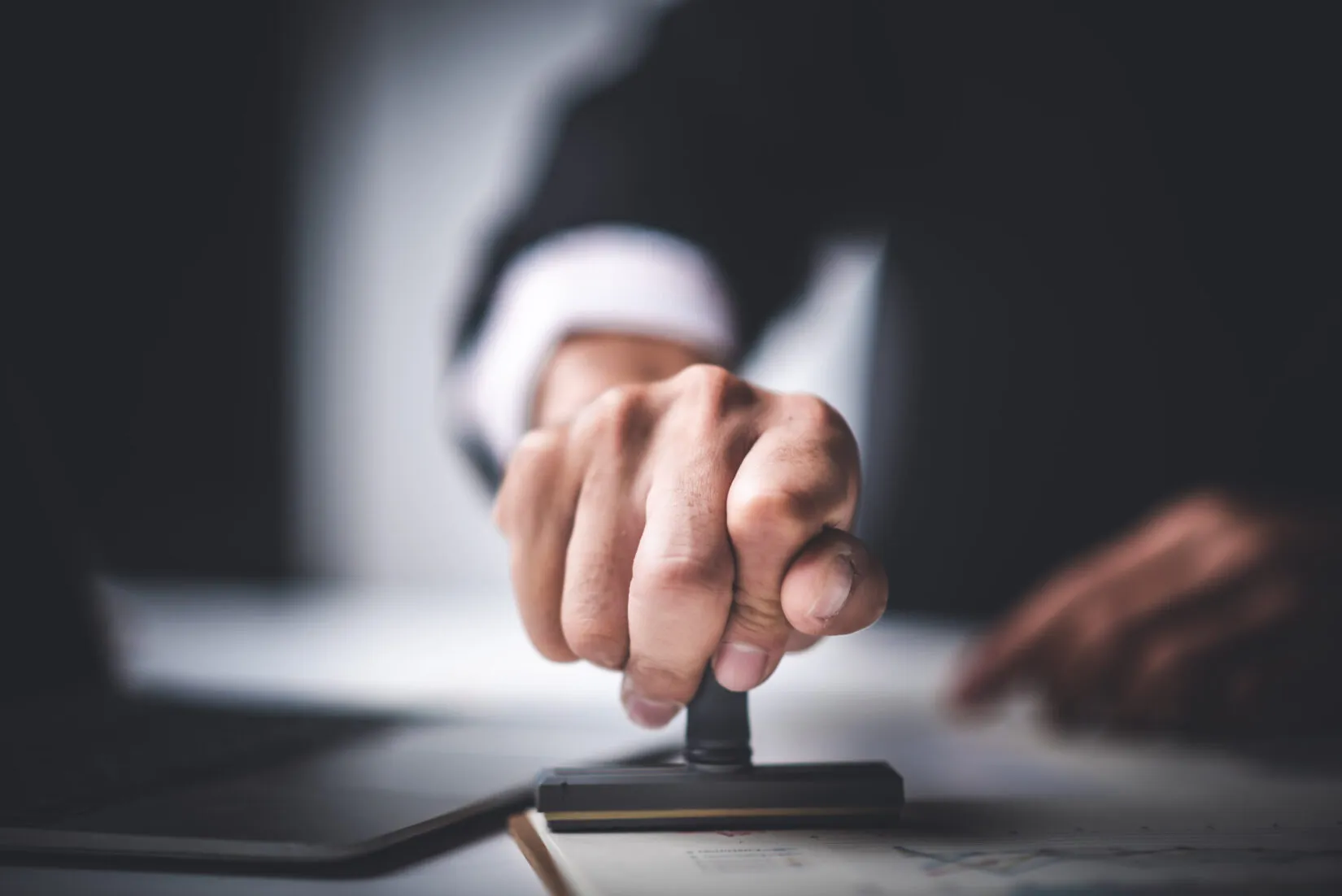 Close-up of a hand pressing a rubber stamp on a document with a blurred background.