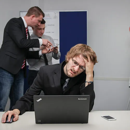 Frustrated man holding his head while sitting at a desk with a laptop.