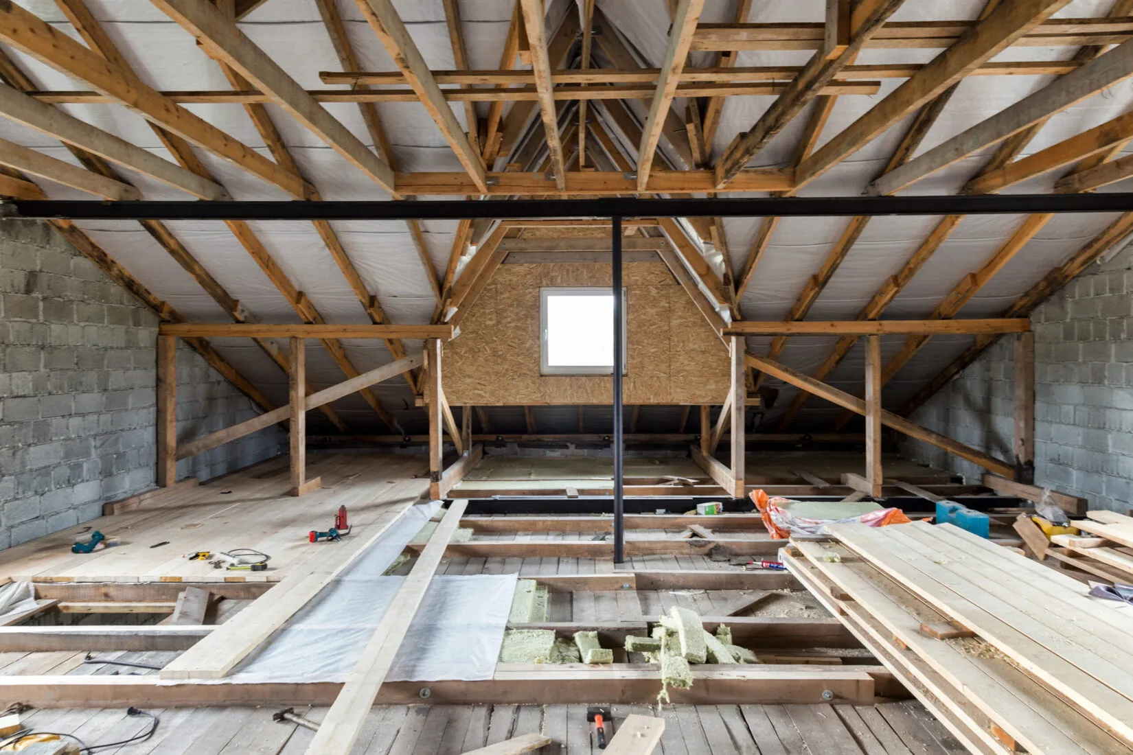 Unfinished attic with wooden beams, insulation, and construction tools scattered on the partially installed floor.