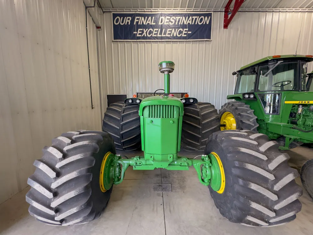 A John Deere 4020 with monster combine wheels sitting in a machine shed. 