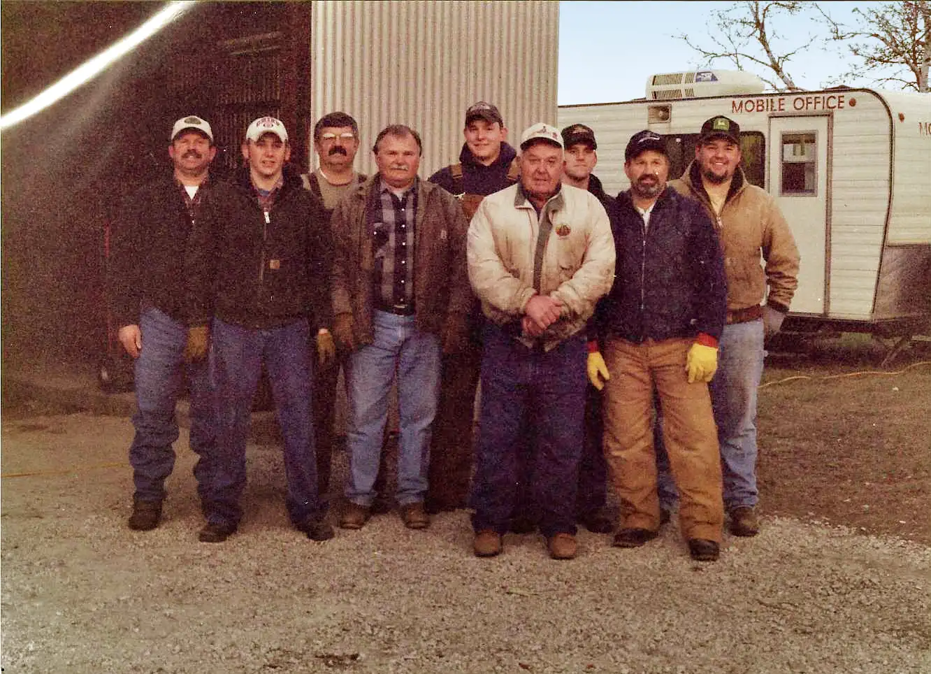 Group of men posing outside in front of a building and a mobile office