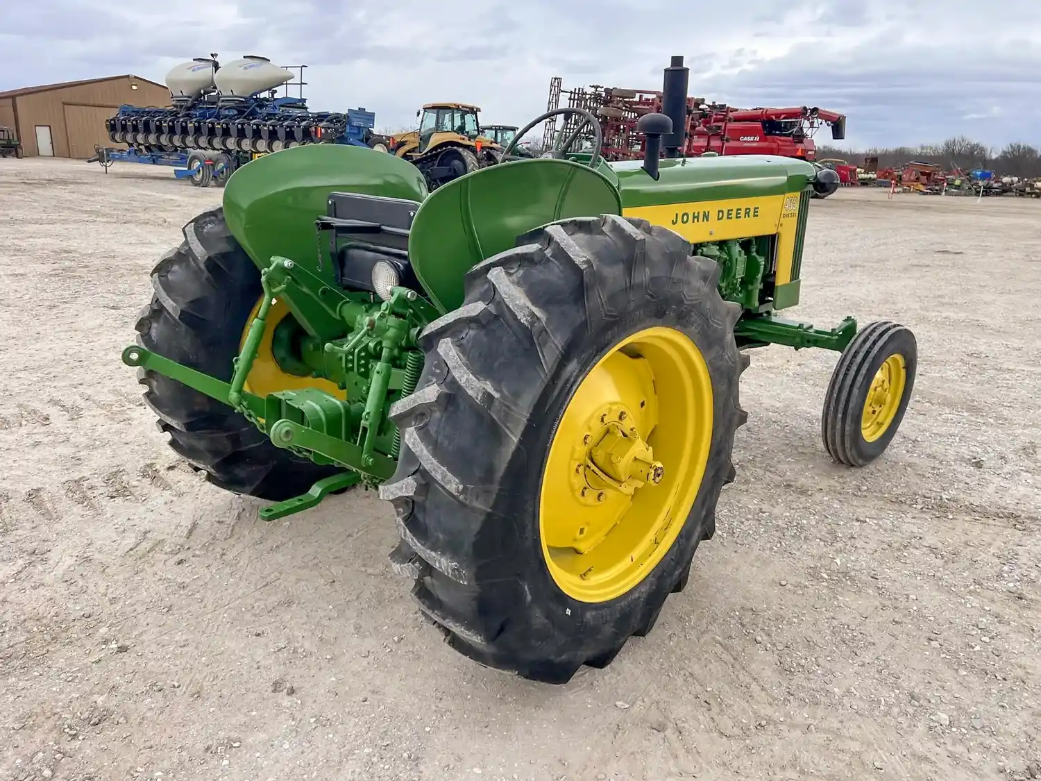 A green farm tractor with yellow wheels parked in a lot with other farming equipment visible in the background