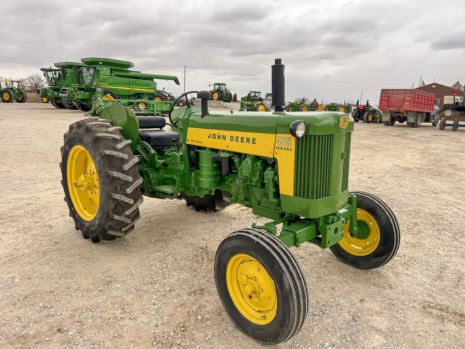 A John Deere tractor displayed on a gravel lot surrounded by other farming equipment in the background
