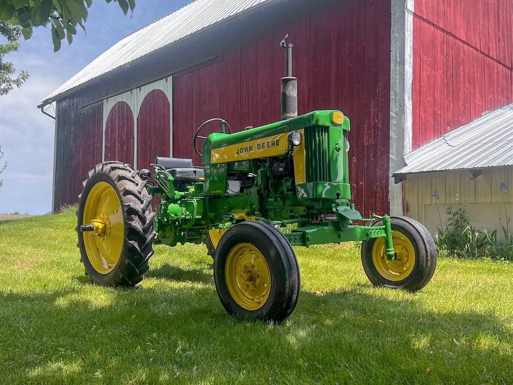 A green tractor on grass near a red barn