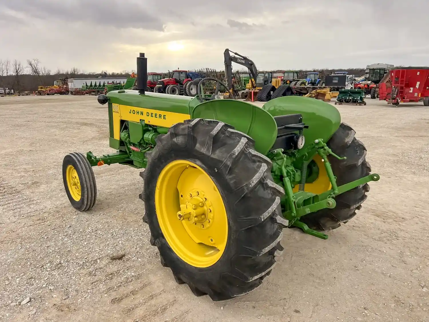 A green and yellow farm tractor parked outdoors on a gravel lot