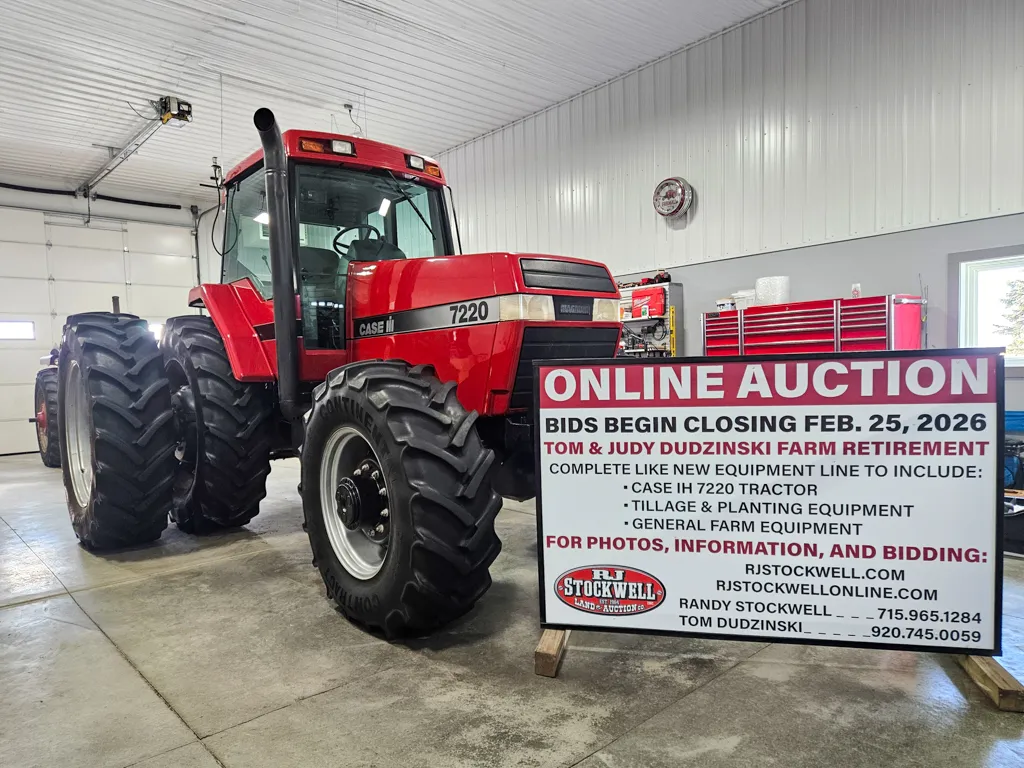 Large red tractor inside a garage next to a sign advertising an online auction for farm equipment