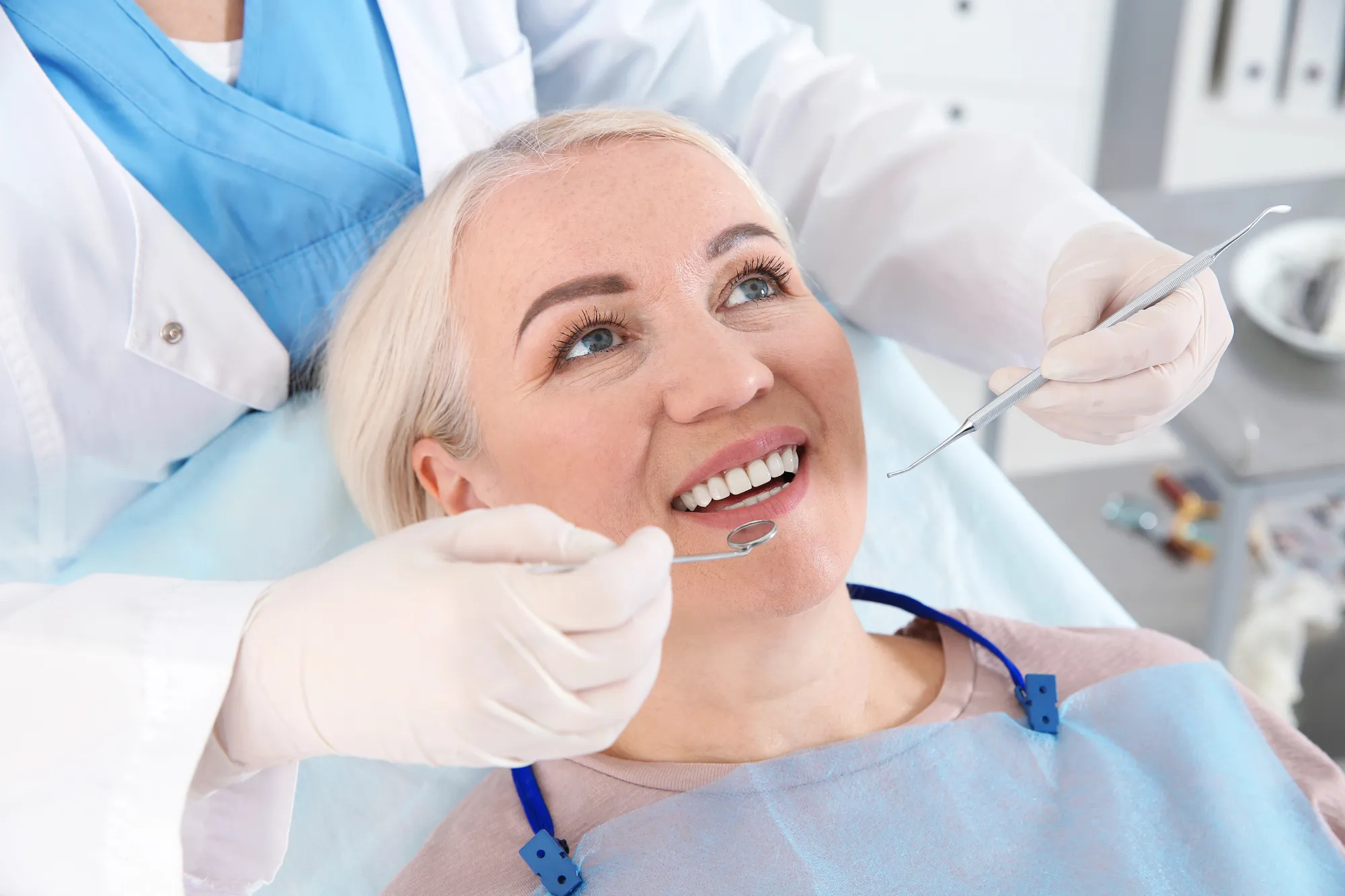 Dentist wearing gloves examining the teeth of a smiling middle-aged woman in a dental clinic.