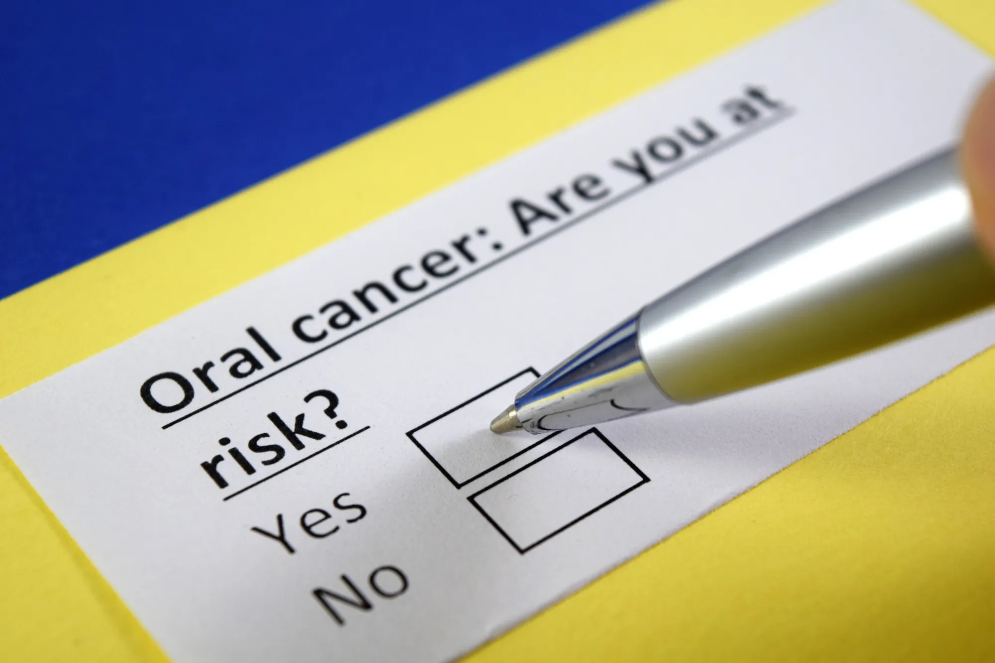 Pen pointing at a checklist about oral cancer risk with options Yes and No on a white card.