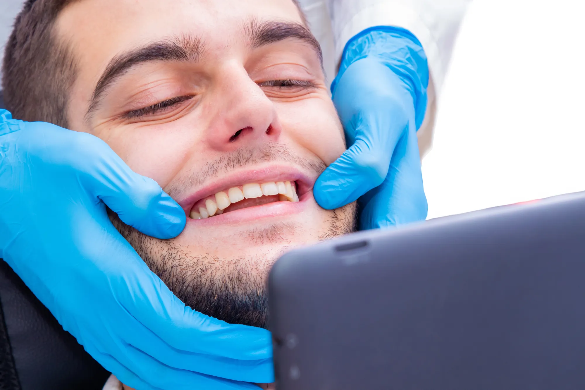 Dentist with blue gloves examining a smiling man's teeth.