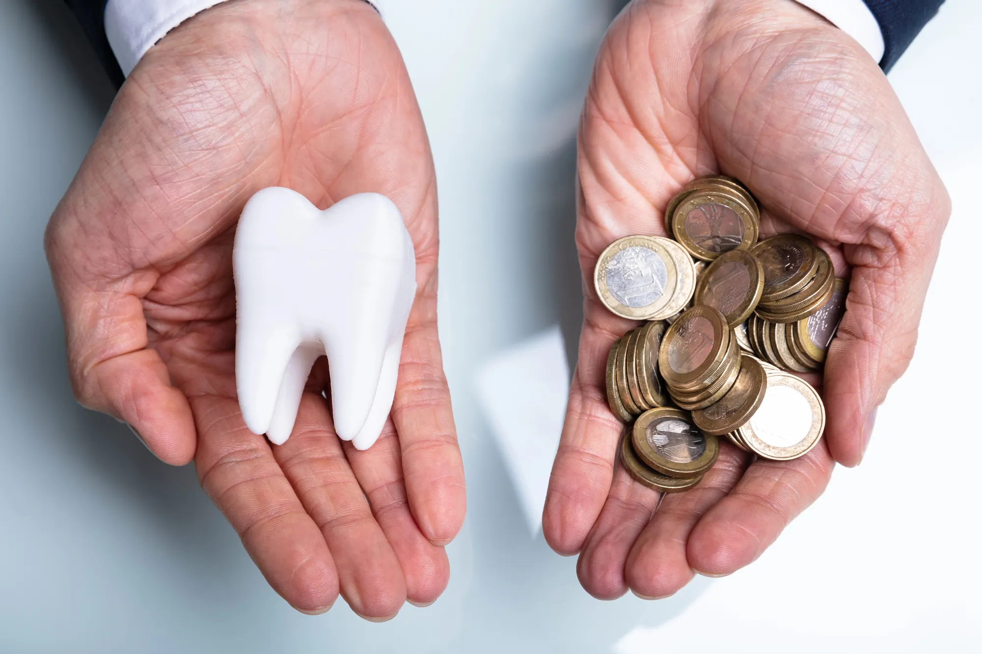 Person holding a white tooth model in one hand and a pile of euro coins in the other.