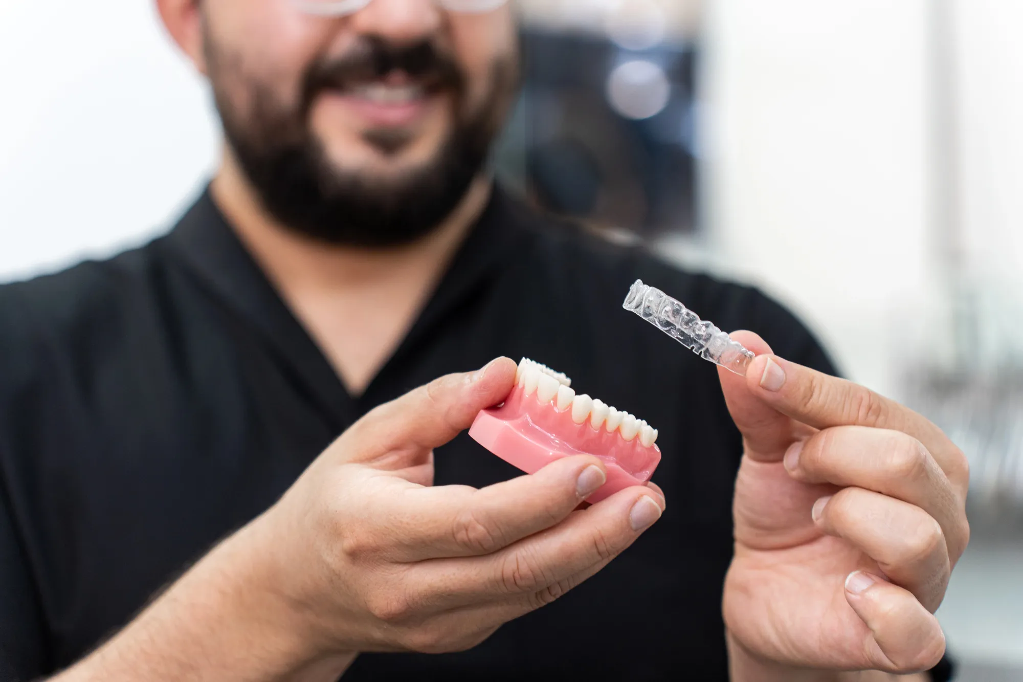 Person holding a dental mold in one hand and a clear dental aligner in the other.