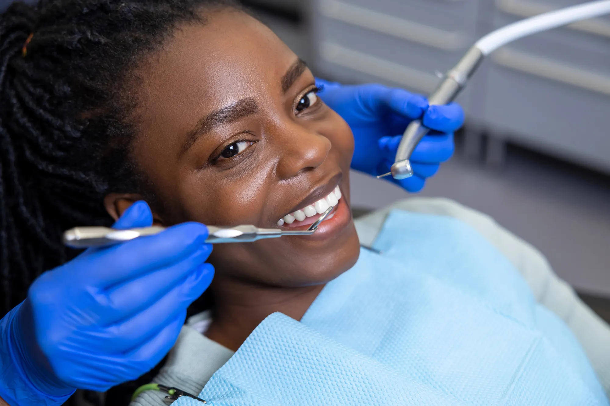 Smiling woman in a dental chair with dentist's gloved hands holding dental tools near her teeth.