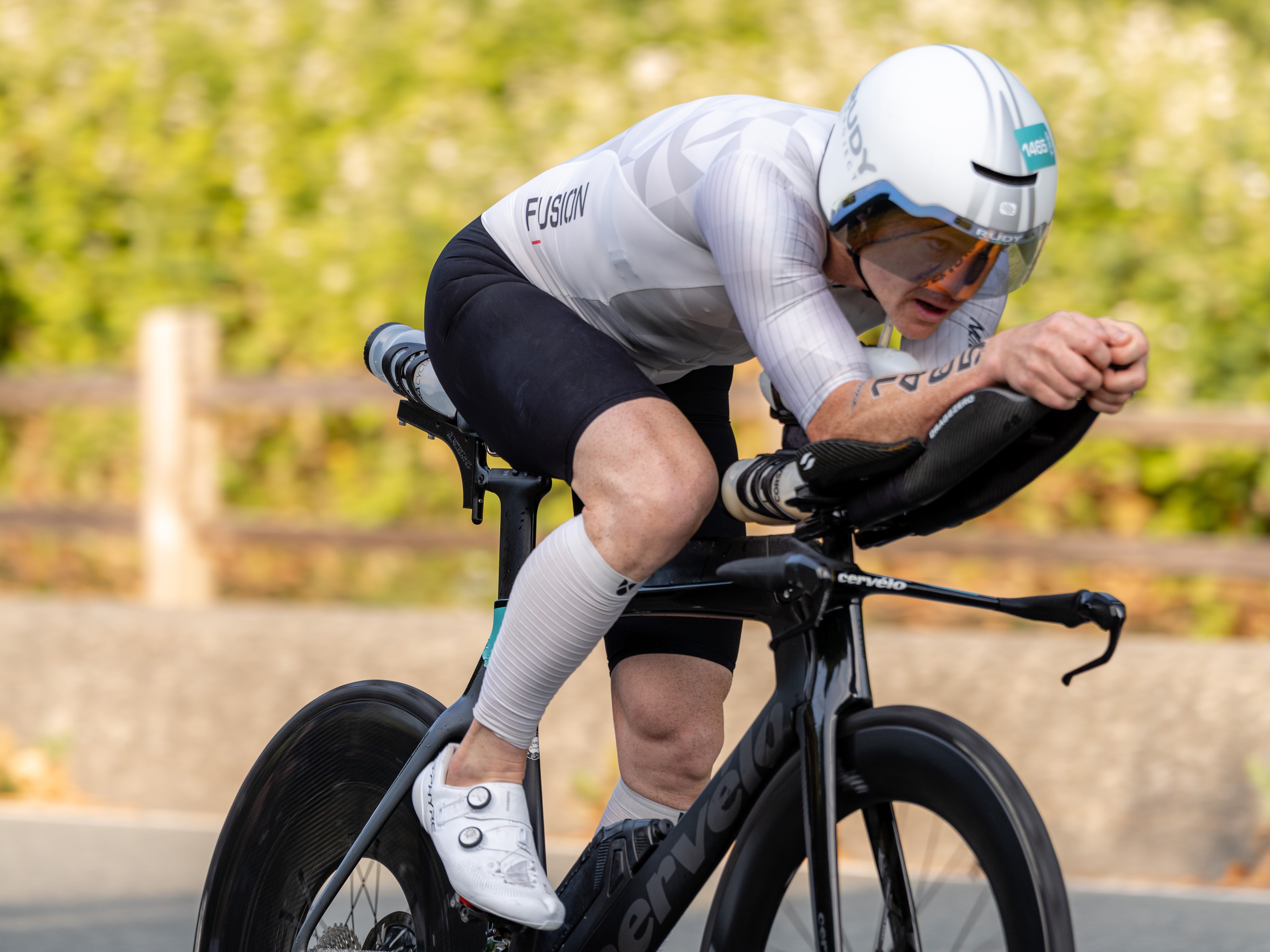 Male cyclist in aerodynamic gear riding a black Cervélo time trial bike on a paved road.