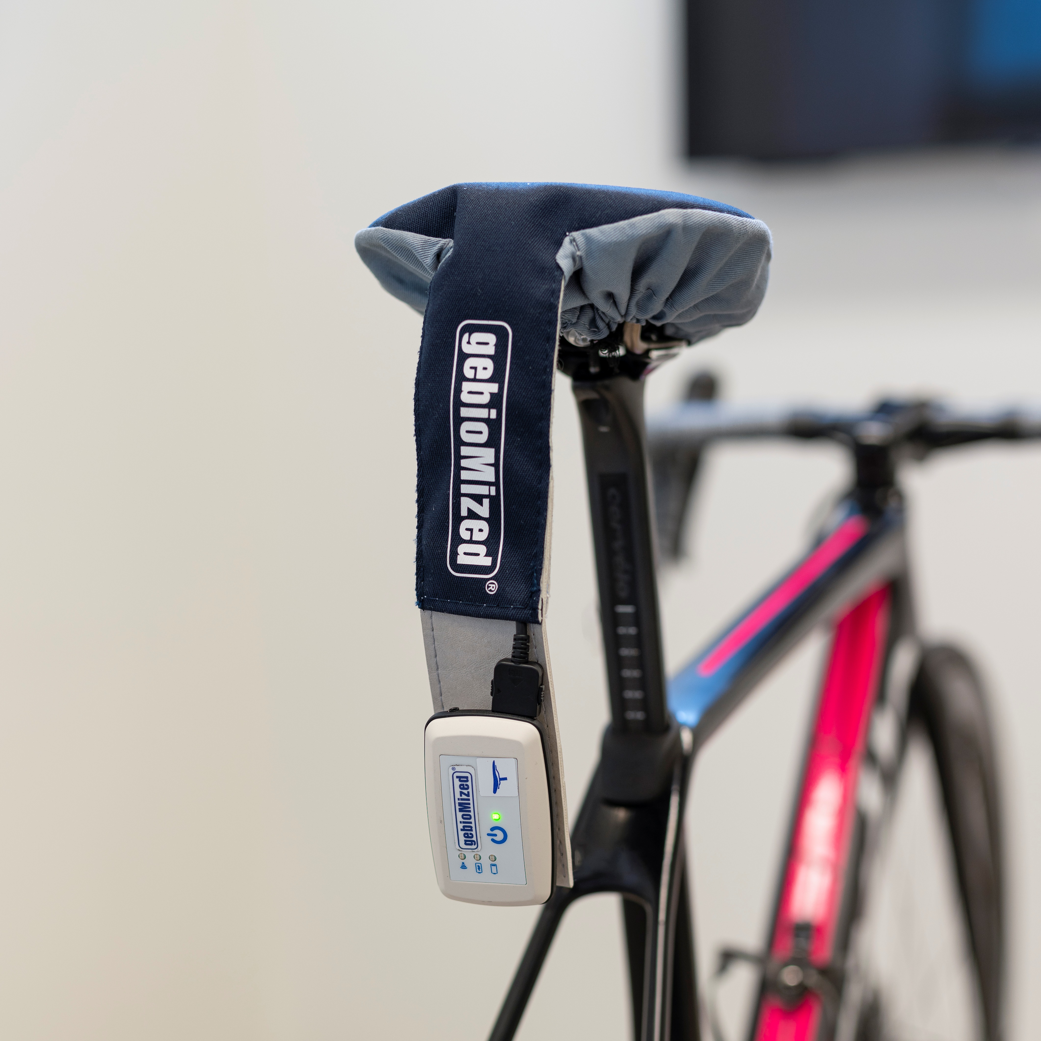 Bicycle saddle with a gebioMized branded strap and an attached electronic device with a glowing green light.