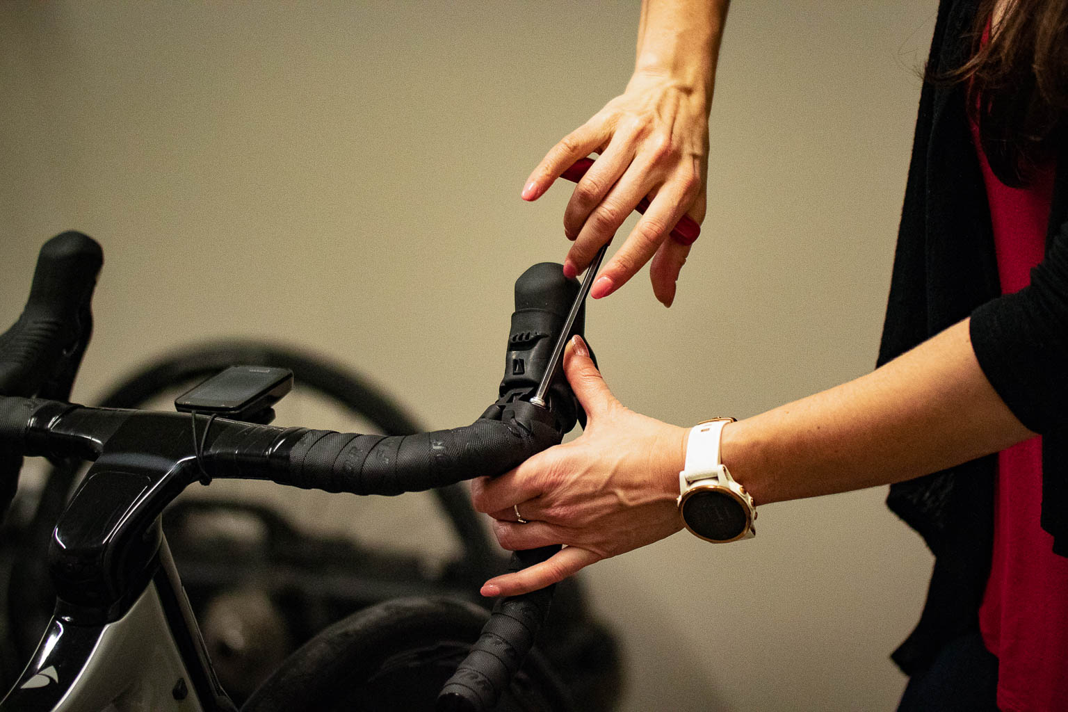 Person using a screwdriver to adjust the handlebar of a black road bike indoors.