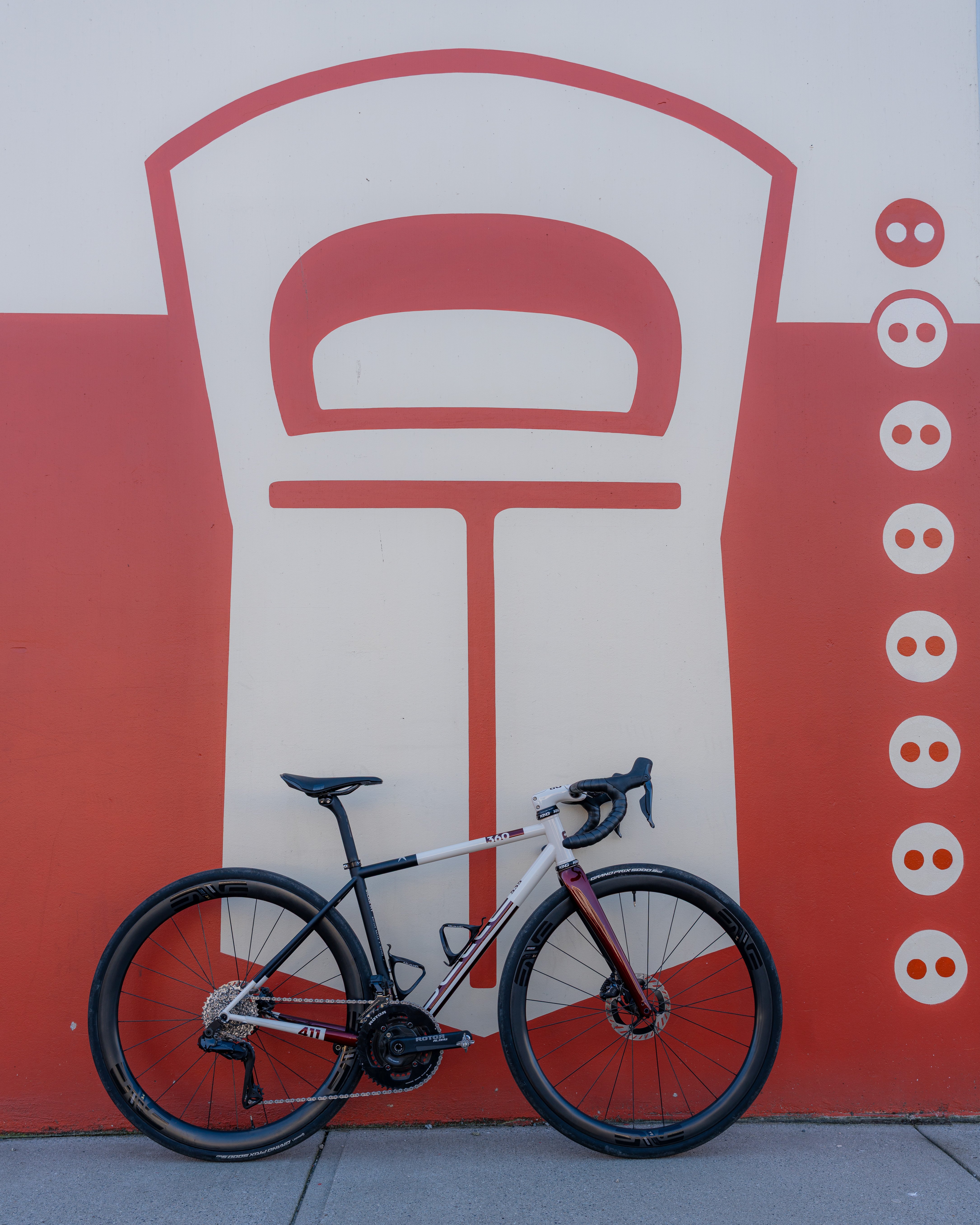 Modern road bicycle with black and white frame leaning against a wall with a large red and white graphic of a stylized bottle opener and circles.