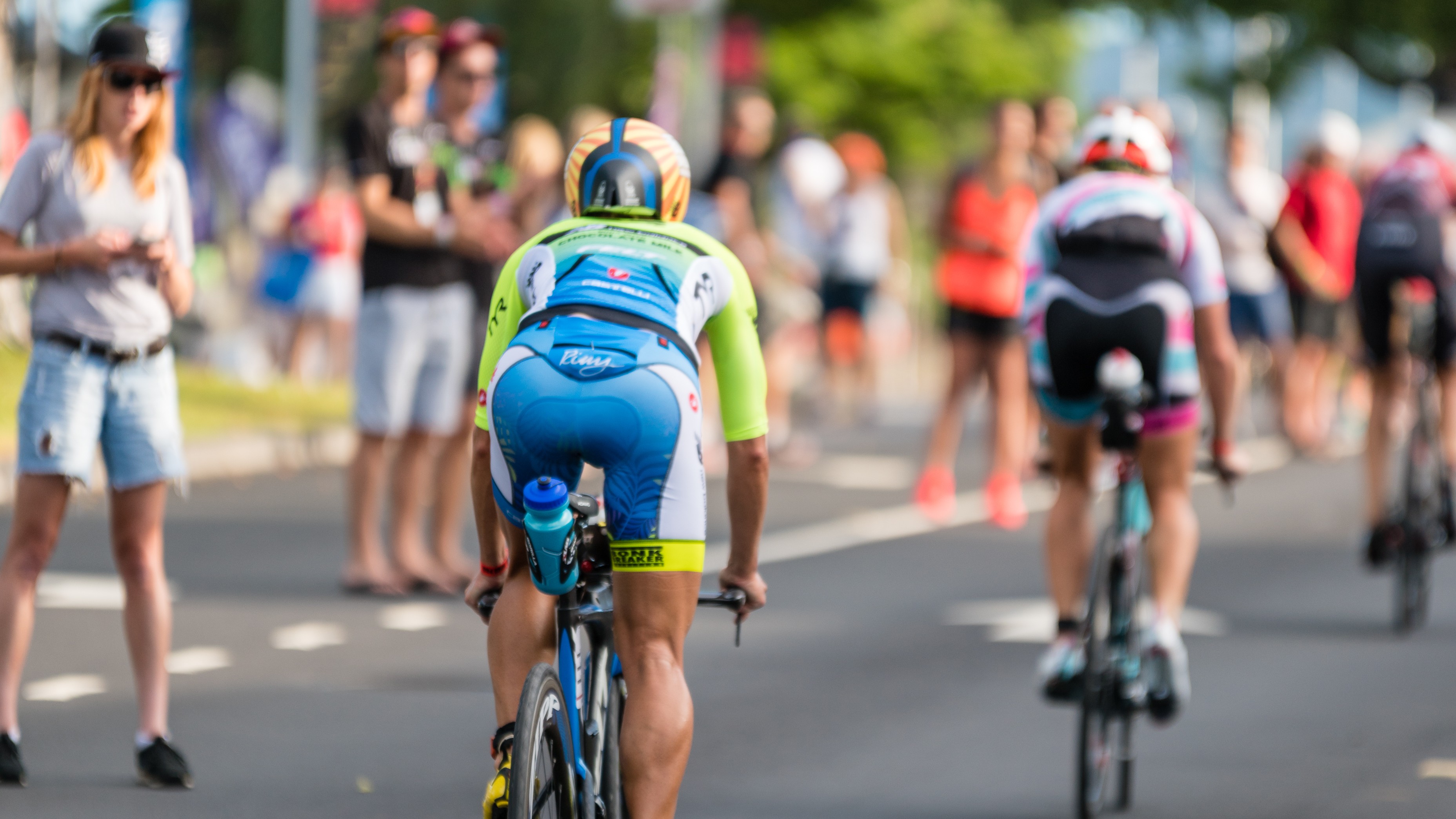 Rear view of cyclists in colorful racing outfits riding on a road with blurred spectators watching.