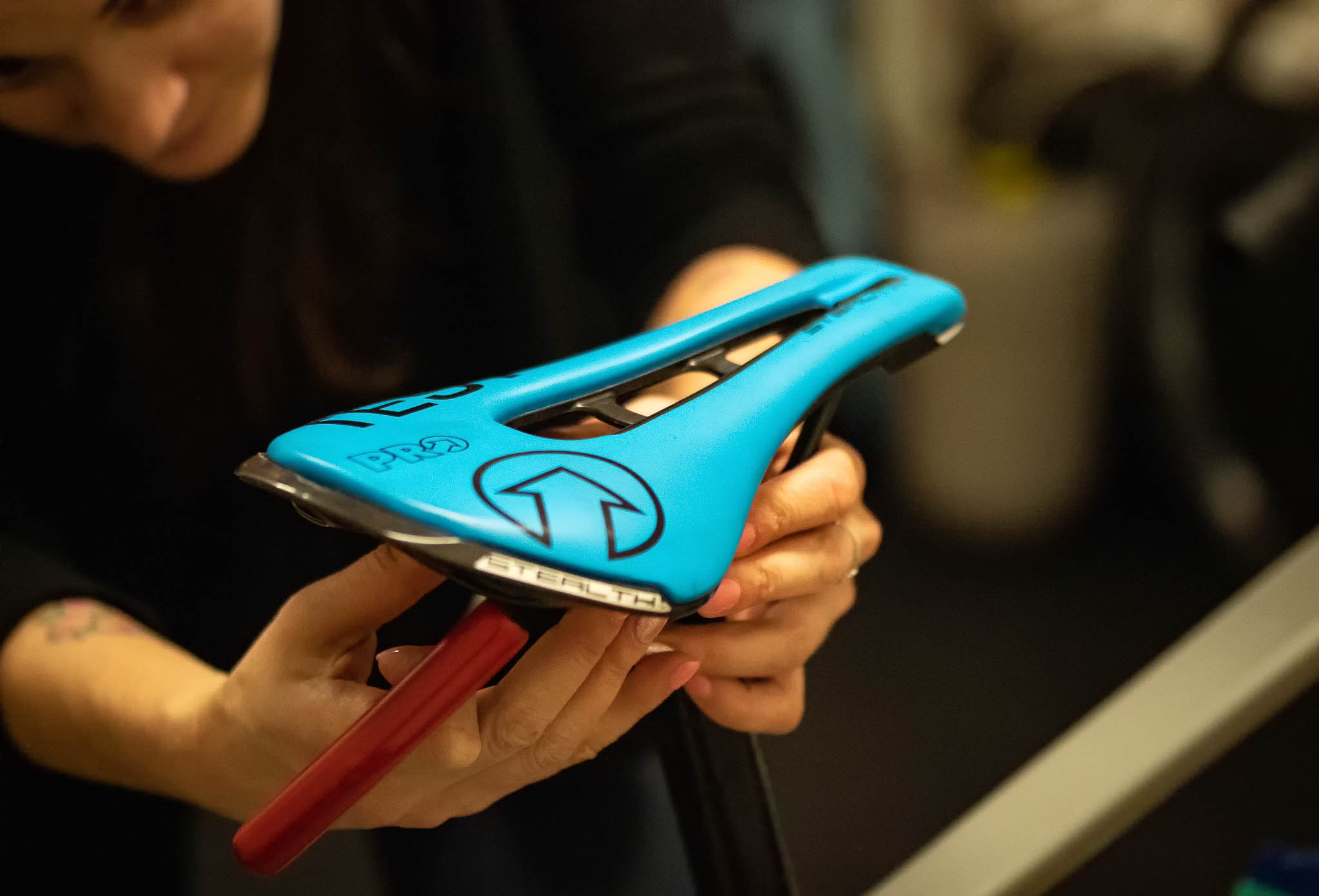 Person holding a blue Selle Italia bicycle saddle with a red attachment rod indoors.