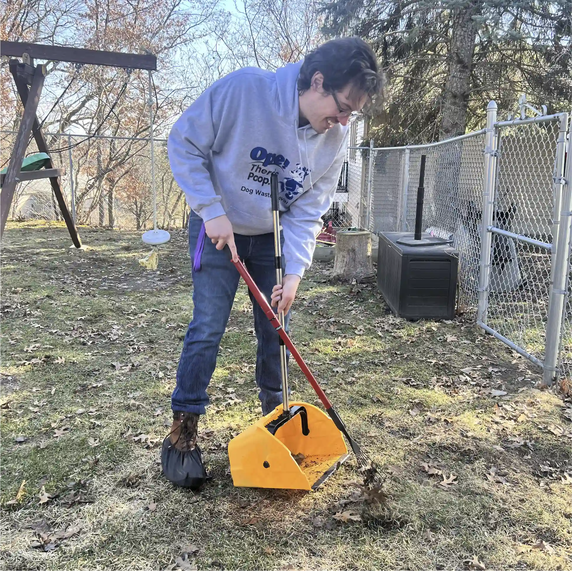 David, the owner of Ope There's Poop in a client's backyard actively scooping dog poop with a yellow pooper scooper. 