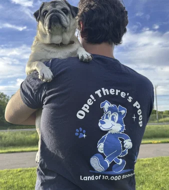 David, the owner of Ope! There's Poop holding Lemon, the pug, while wearing the pooper scooper t-shirt. 
