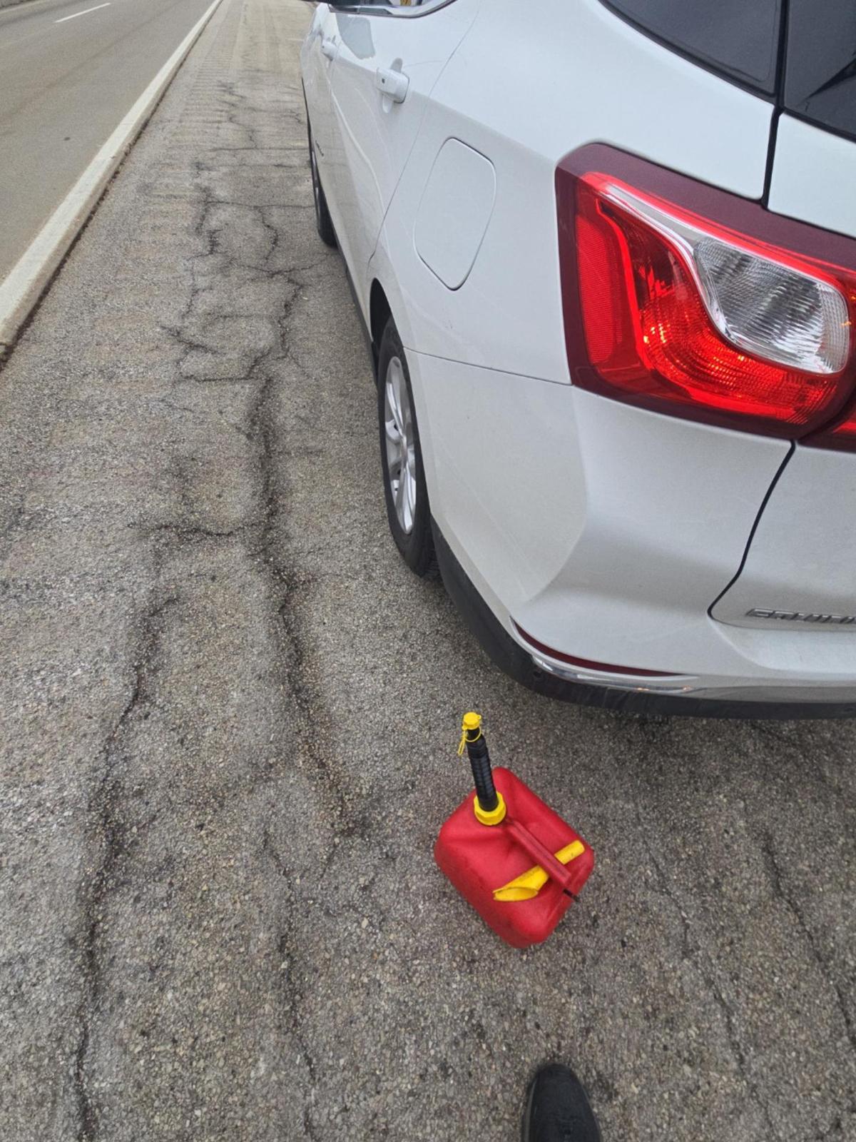 White car parked on a rough cracked road with a red gas can on the ground near the rear tire.