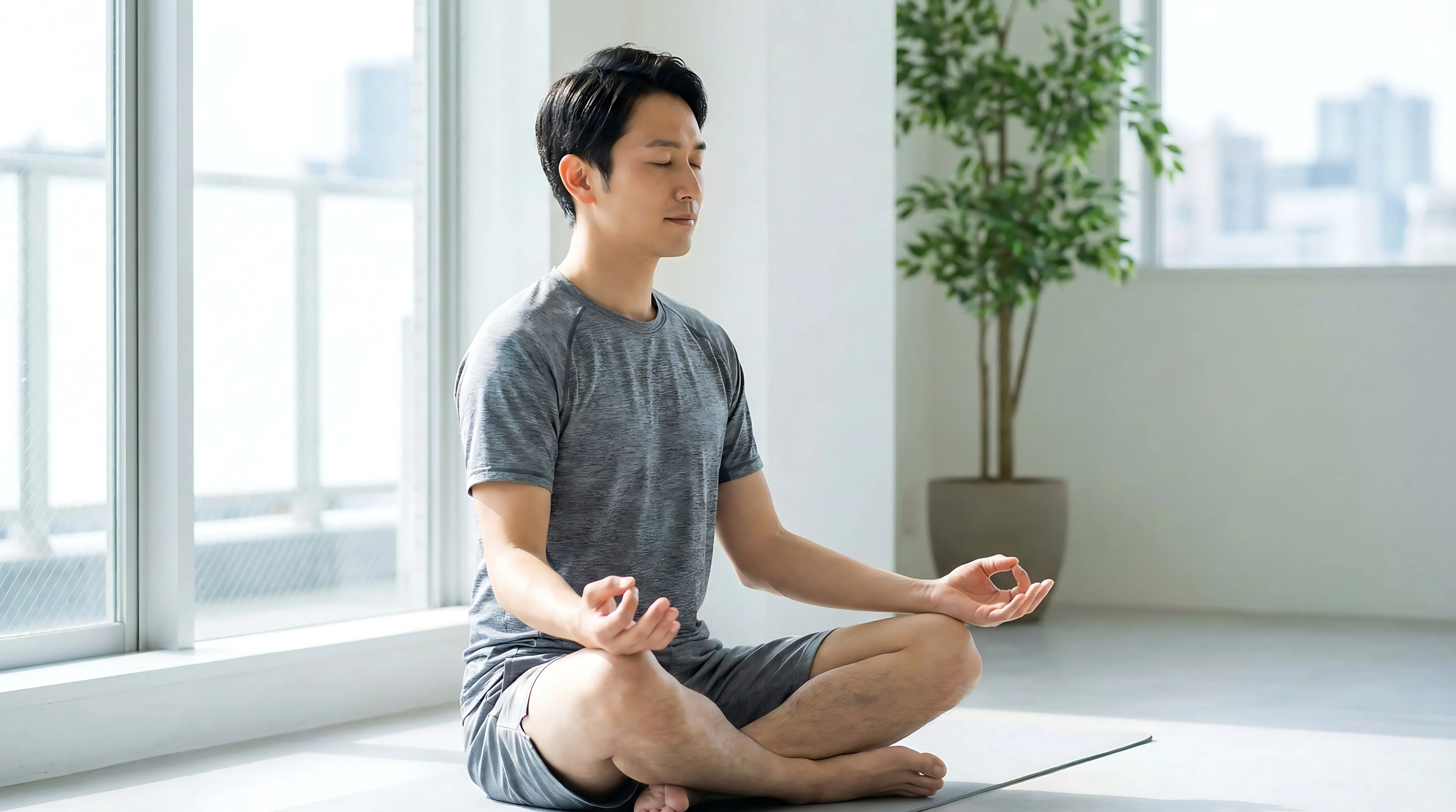 屋内で静かに座り瞑想するグレーのスポーツウェアを着た男性。
