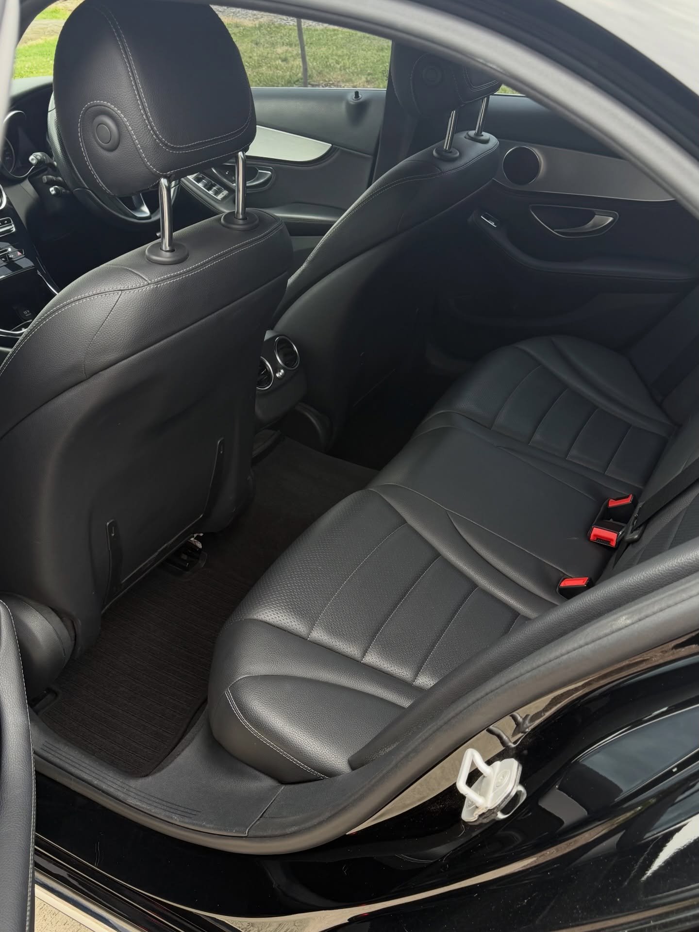 Interior view of a car's backseat with black leather seats, seatbelt buckles, and front seat backs visible.