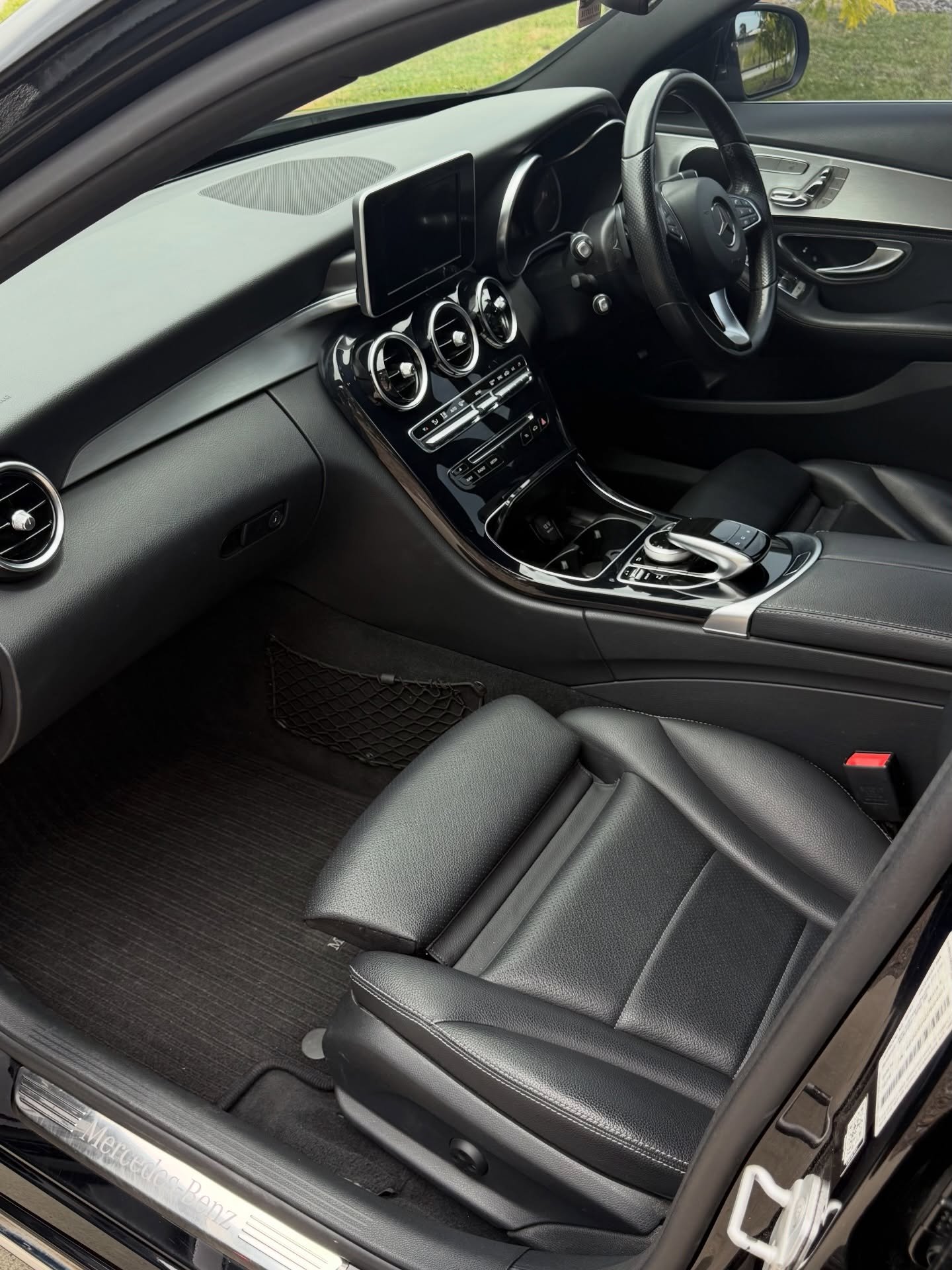 Interior of a Mercedes-Benz car showing black leather passenger seat, dashboard with three circular air vents, center console with controls, and door panel.
