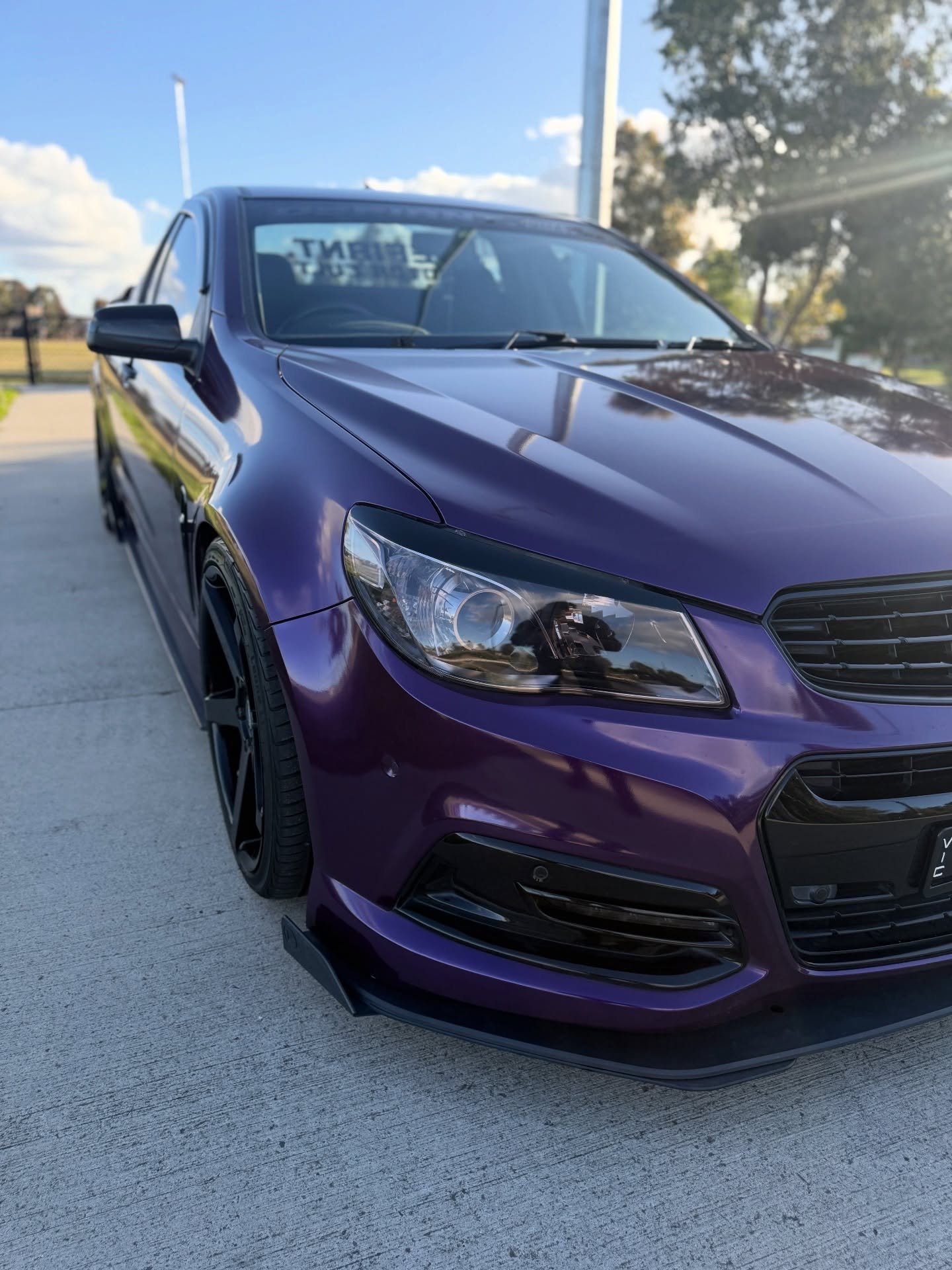 Front-left view of a shiny purple sedan with black rims parked on a concrete driveway under a blue sky.