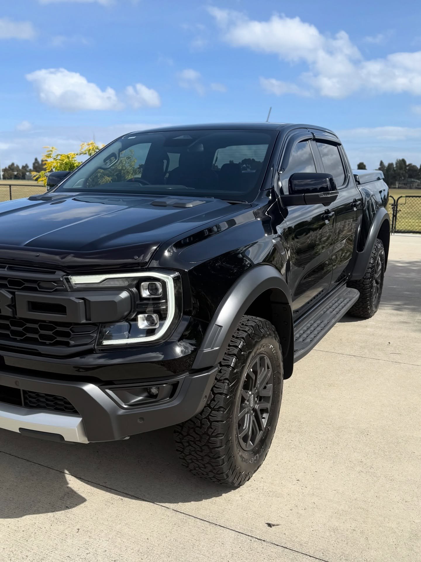 Black Ford pickup truck parked on concrete under a partly cloudy sky.