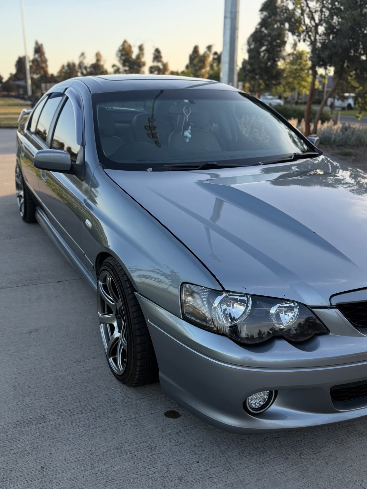 Silver sedan parked on concrete with tinted windows and custom rims in a suburban setting at sunset.