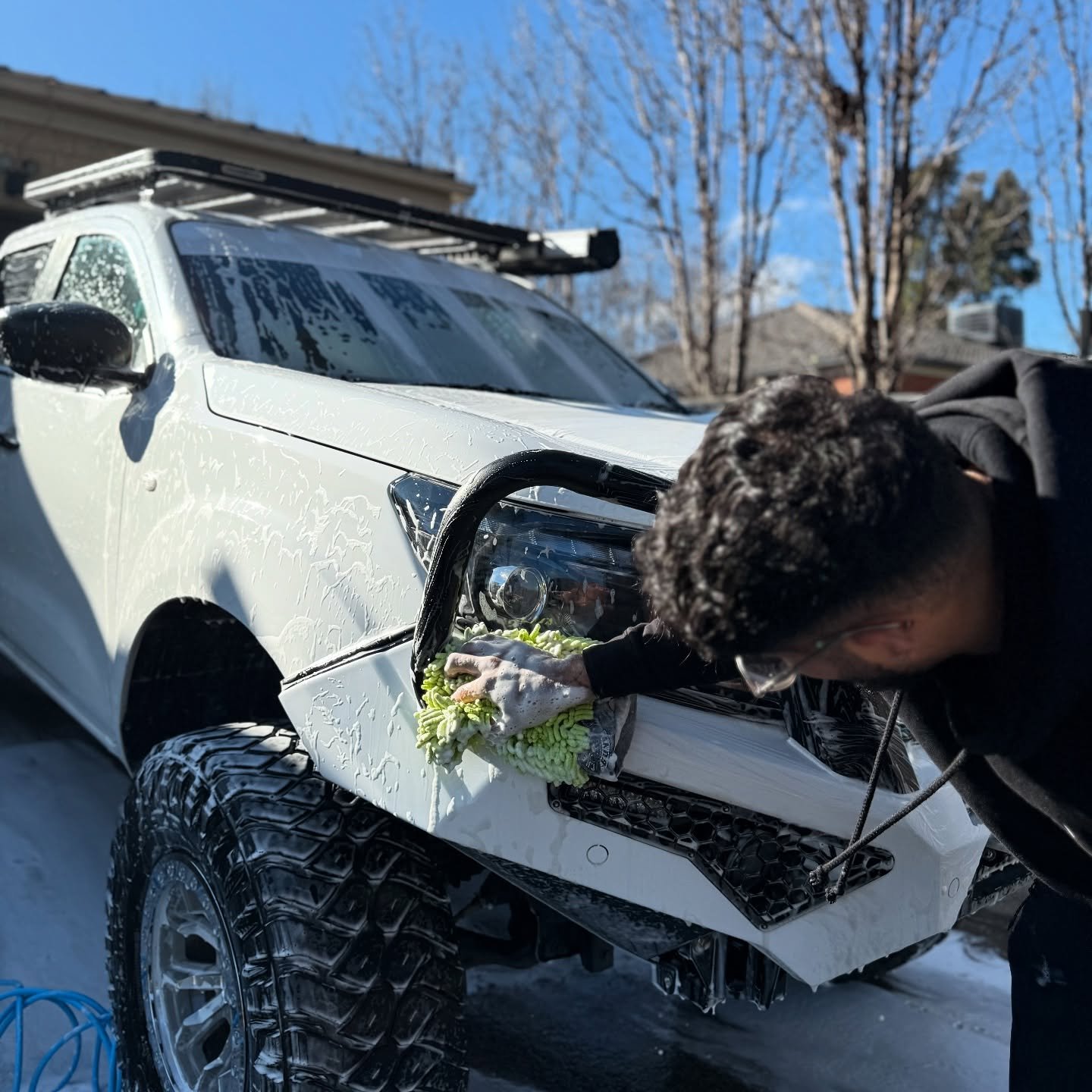 Person cleaning the front headlight of a white off-road vehicle with a green microfiber cloth on a sunny day.