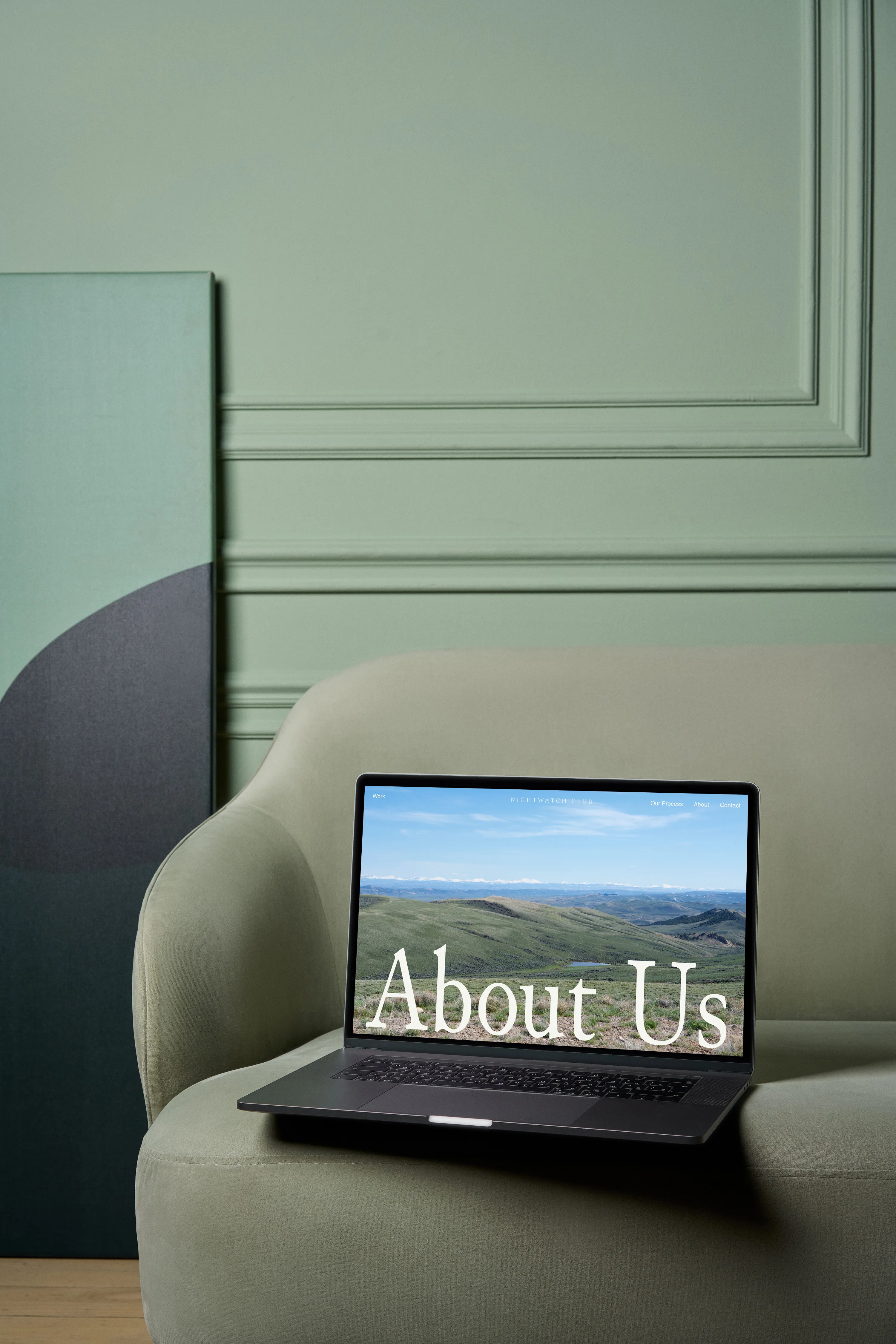 A laptop resting on a green sofa displaying the nightwatch website