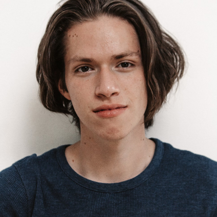 Young man with medium-length brown hair wearing a dark blue shirt, facing forward with a neutral expression.