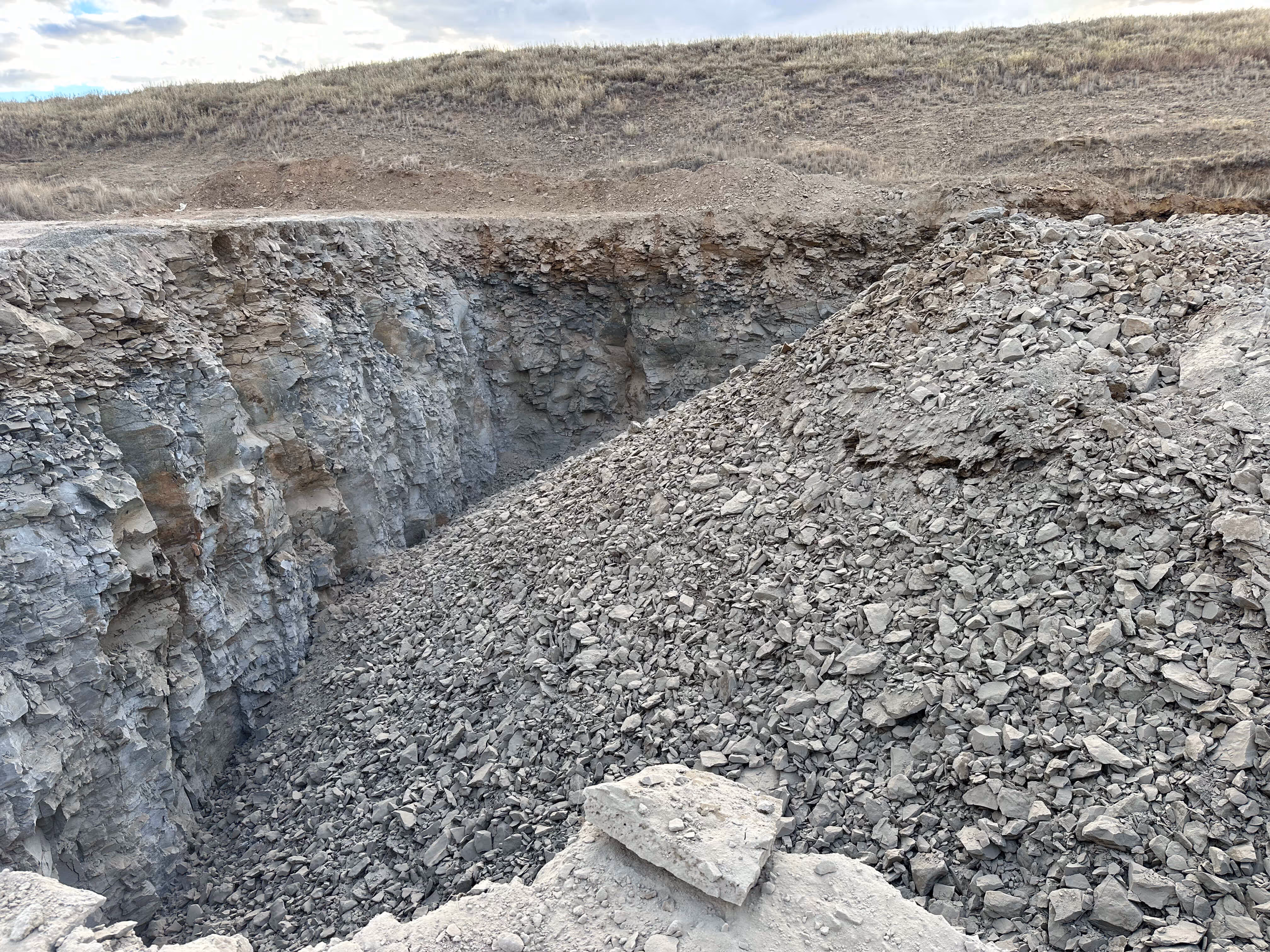 Large quarry pit filled with loose grey rocks and cliffs of exposed stone under a cloudy sky.