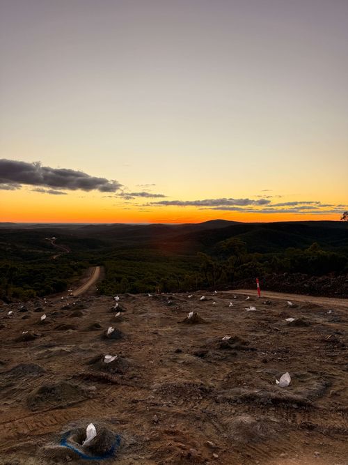 Sunset with vibrant orange and purple clouds over a barren landscape featuring a white vehicle marked with 'EXPLOSIVES'.