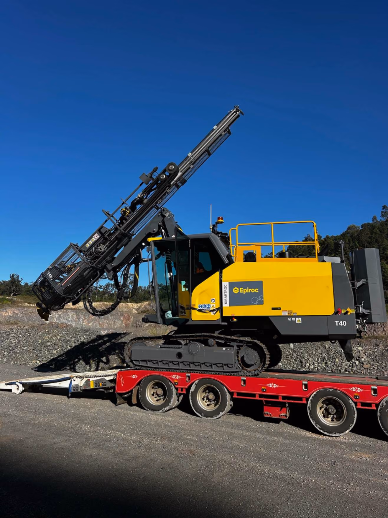 Yellow and black Epiroc T40 drilling machine on a red flatbed trailer in a rocky outdoor area.