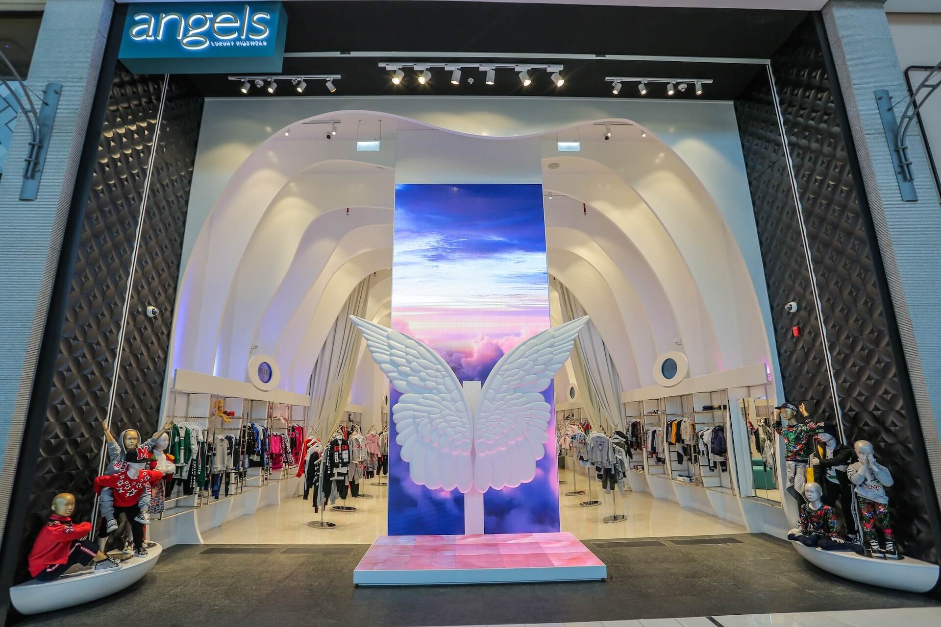 Angels fashion store display with angelic wings and sky imagery on screen and mannequins