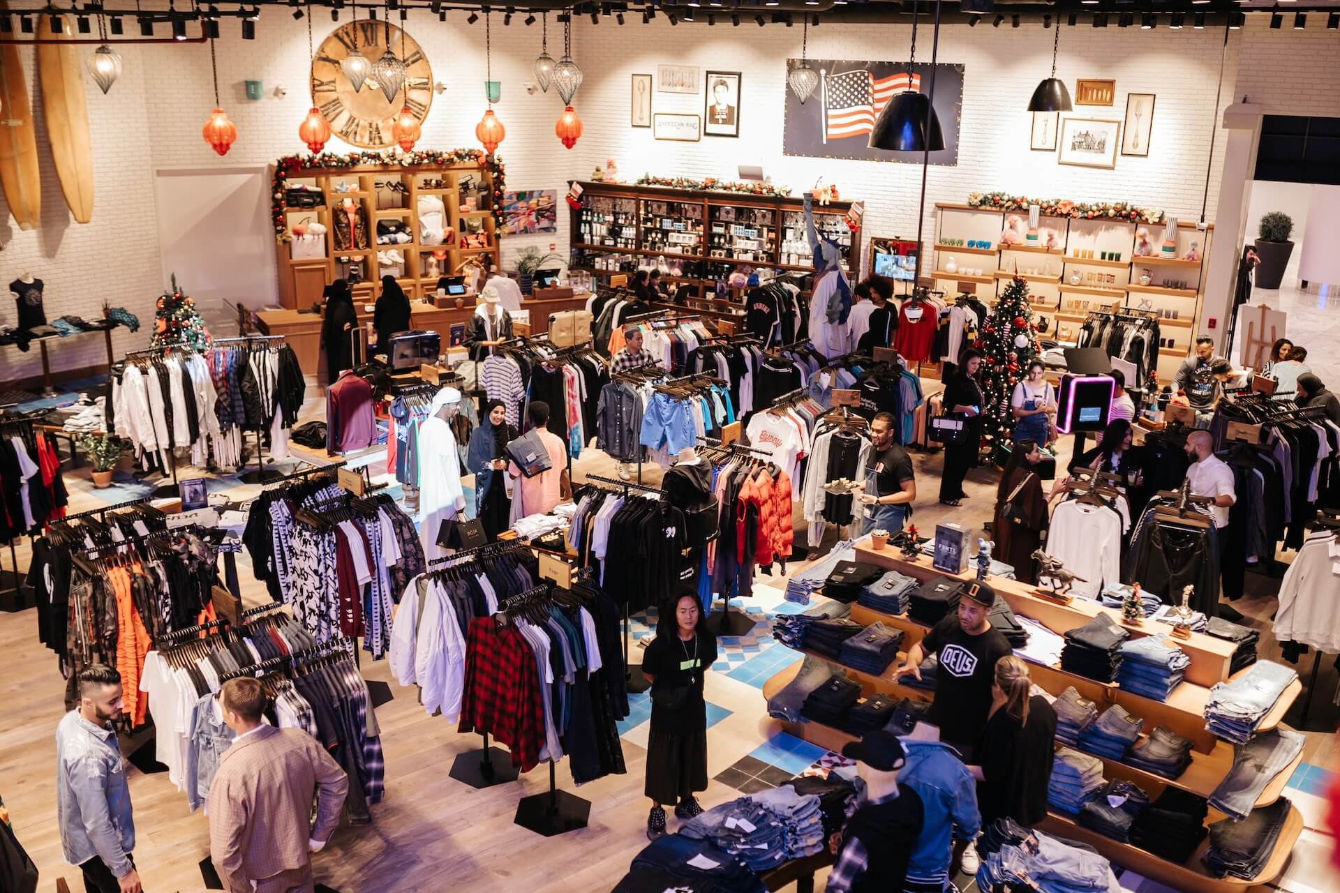 Busy clothing retail store interior with shoppers browsing merchandise and holiday decorations.