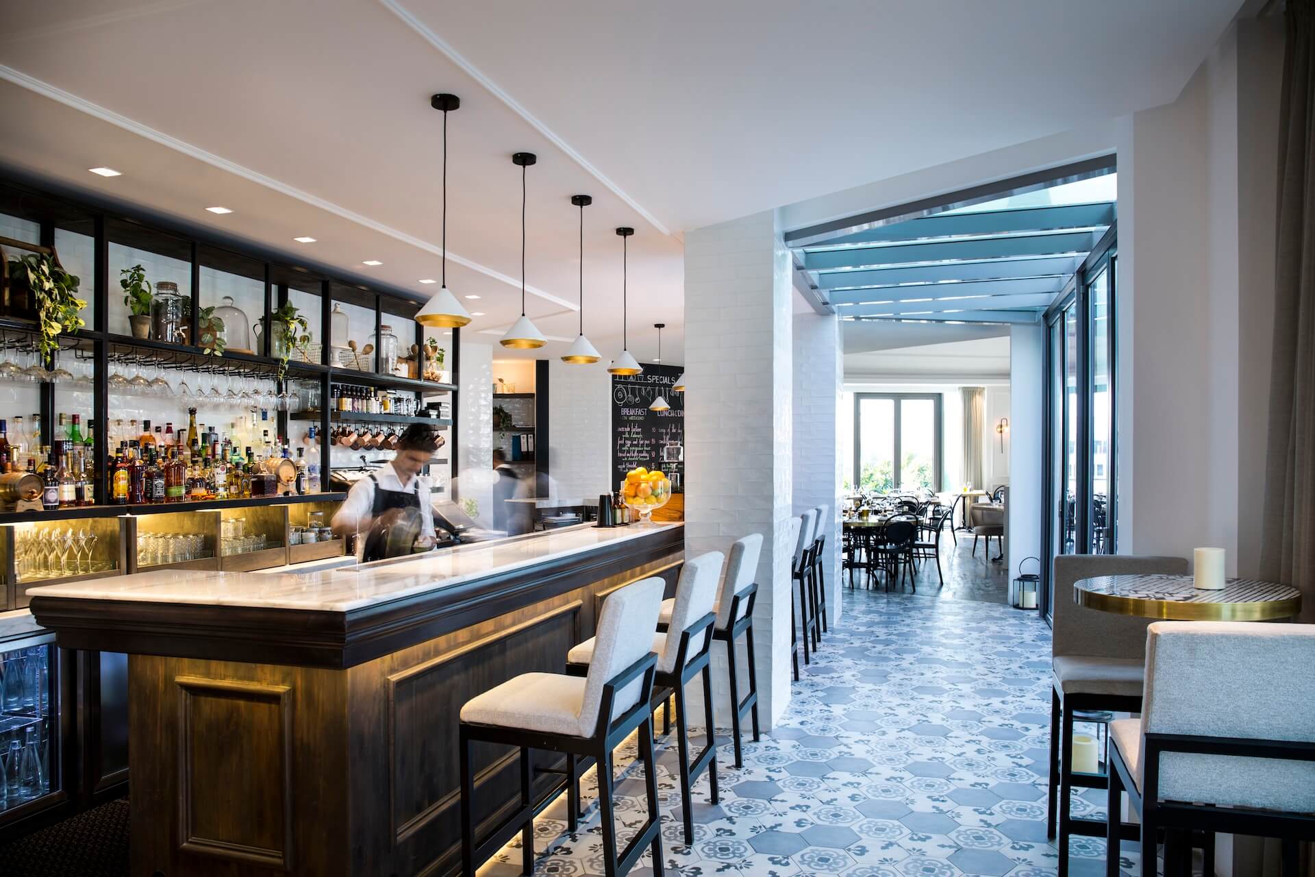 Modern bar and restaurant interior with bartender, pendant lighting, and dining area visible