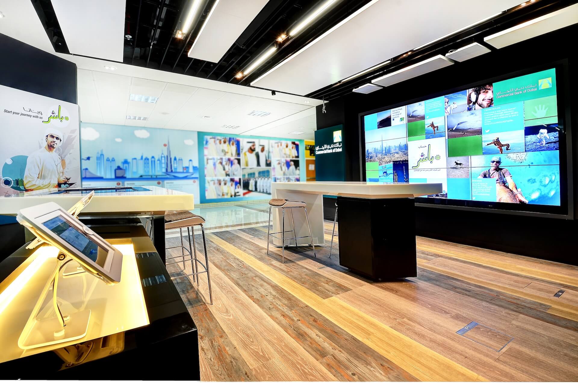 Modern exhibition space with digital displays, counter, and multiple video screens showing tourism content.