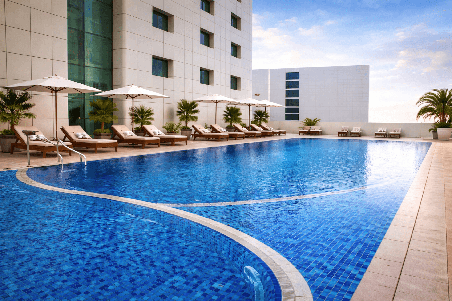 Luxury resort swimming pool with lounge chairs, umbrellas, and modern building