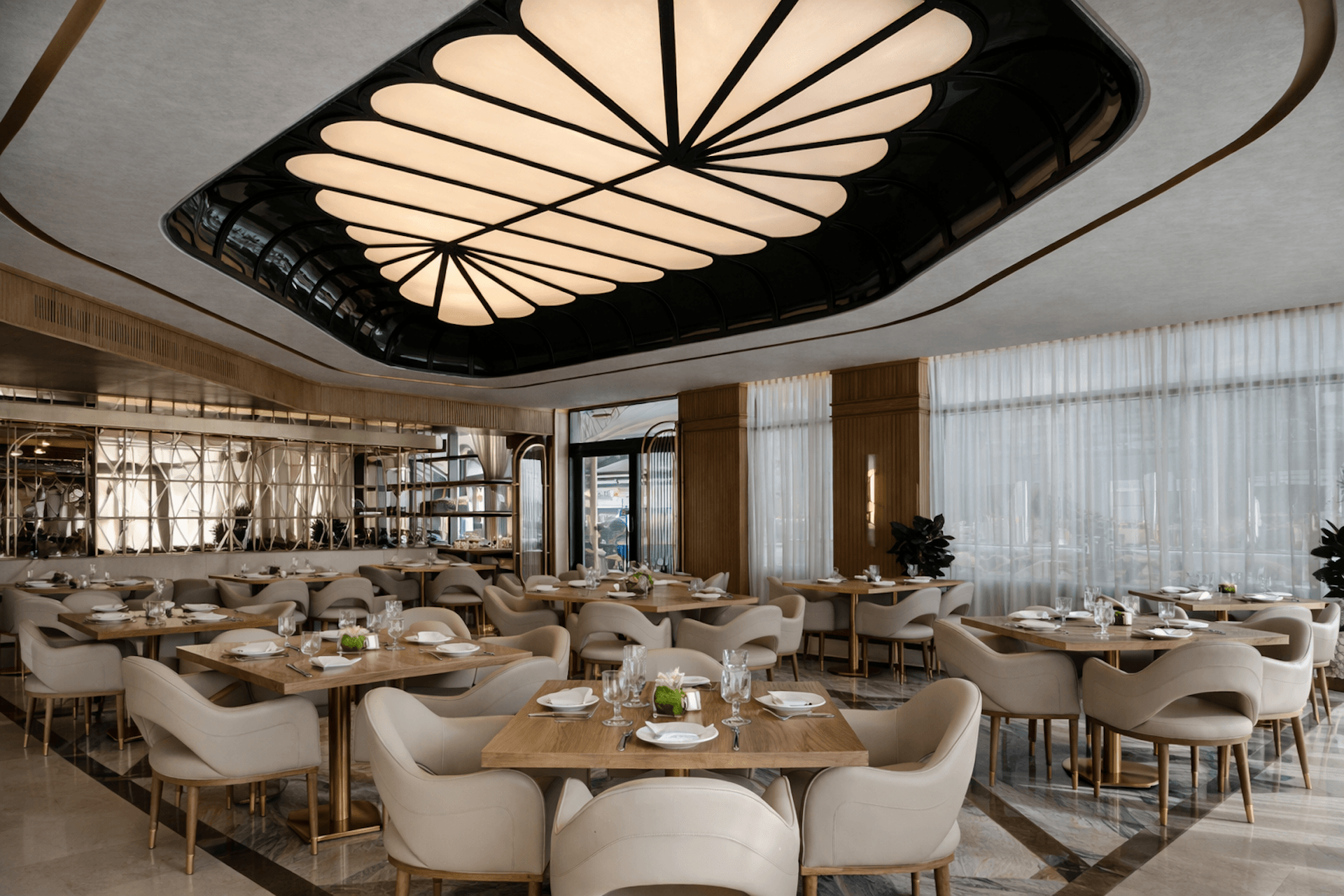 Modern restaurant interior with wing-shaped ceiling light, wooden tables, and cream chairs.