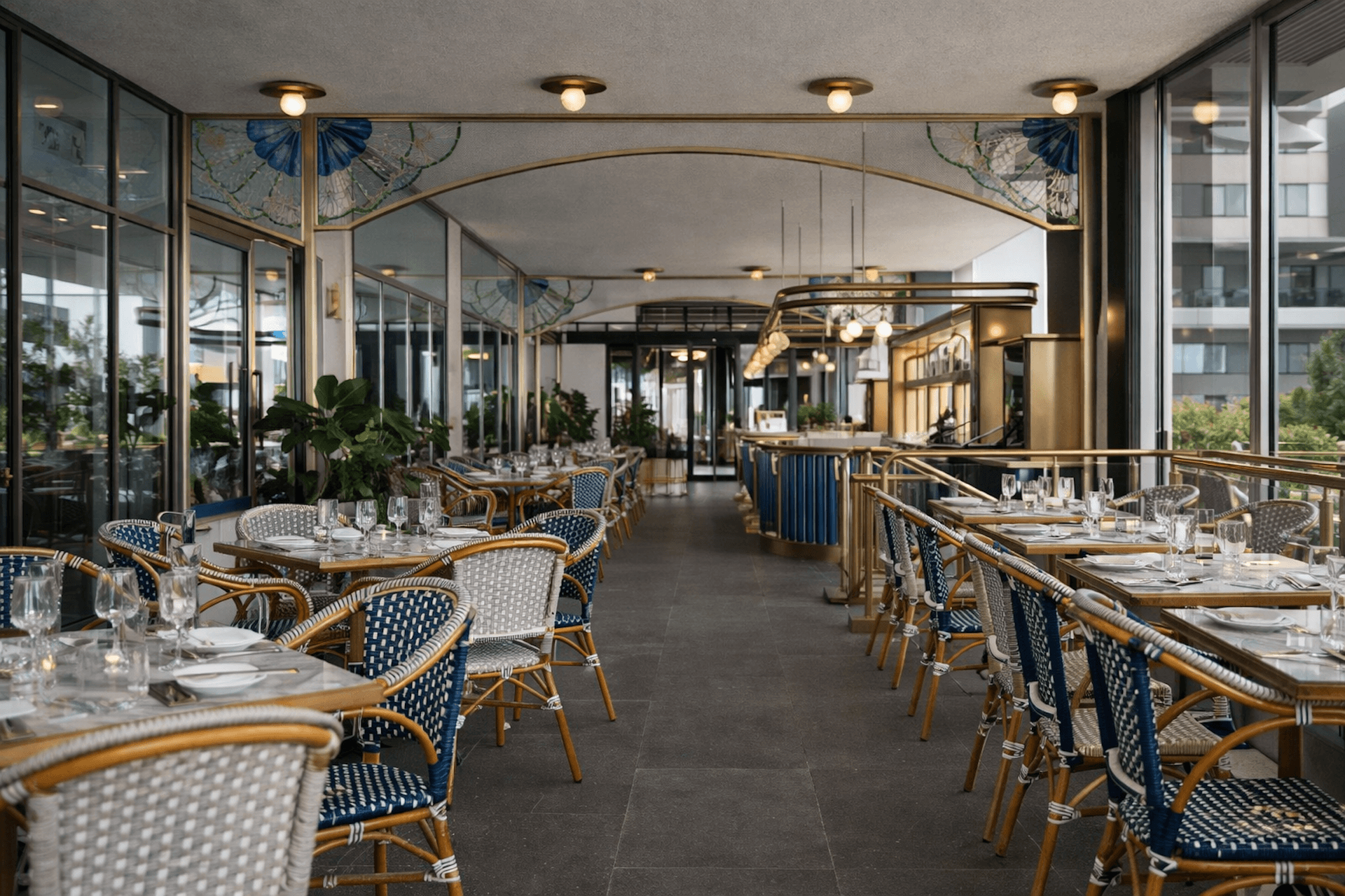 Elegant modern restaurant terrace with wicker chairs, set tables, and blue decorative accents.