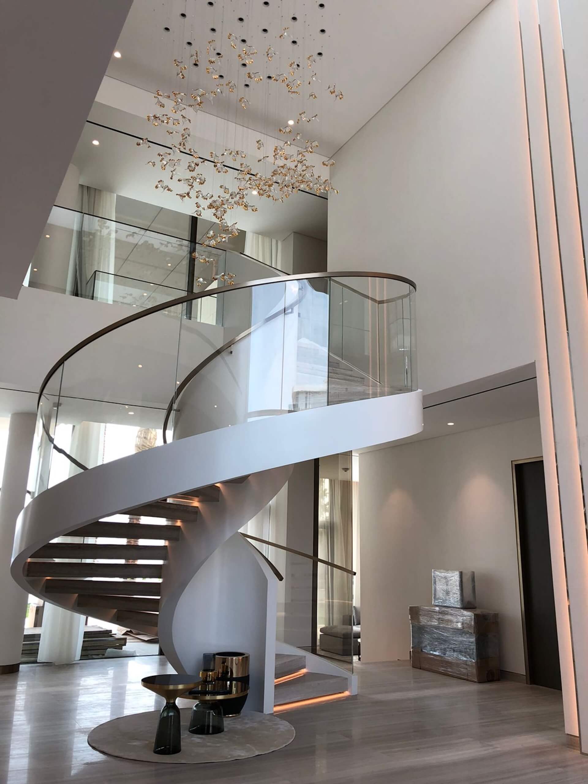 Modern spiral staircase with glass railing in luxury multi-level foyer with chandelier
